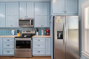 A kitchen with light blue cabinets, stainless steel appliances, a microwave, oven, and a refrigerator with a water dispenser. - Bella Costa by Miss Kitty’s (Rockport)
