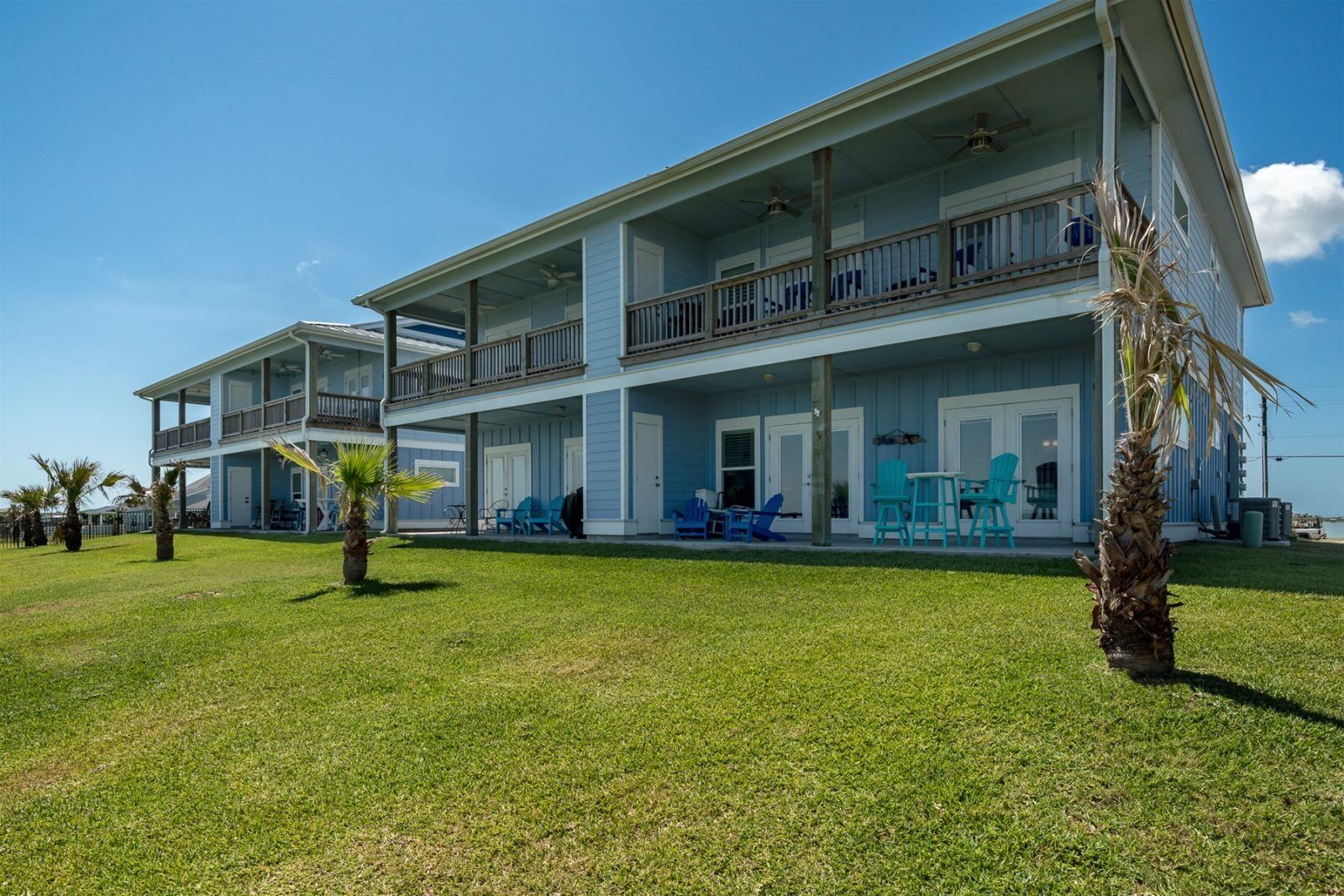 A two-story beachfront property with a covered patio, outdoor seating, and a view of the ocean.