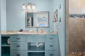 A bathroom with a marble countertop, a sink with a mirror, and a towel rack. - Bella Costa by Miss Kitty’s (Rockport)