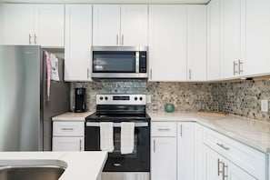 A kitchen with white cabinets, a stainless steel refrigerator, a microwave, and a stove.