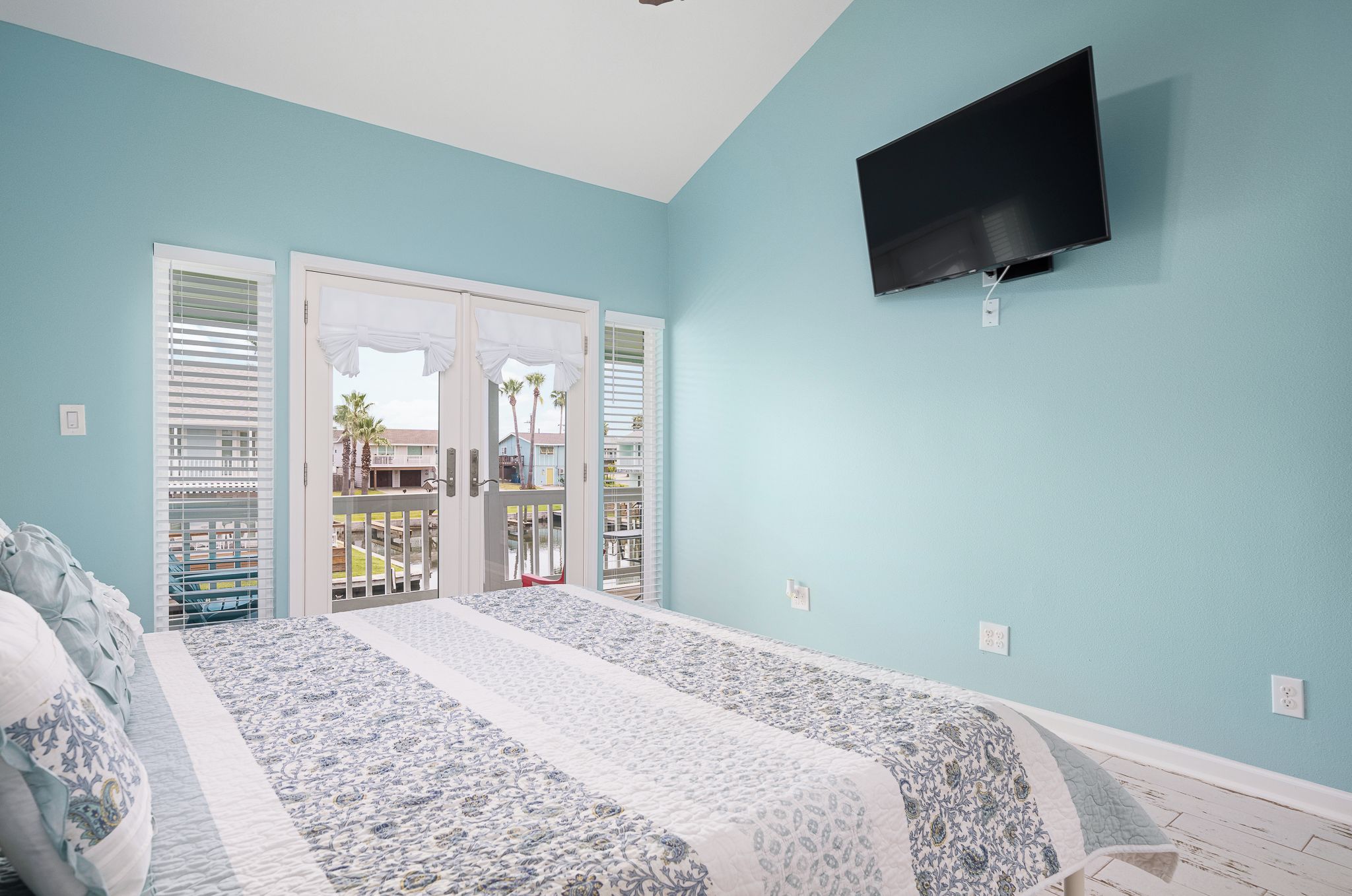 A bedroom with a bed, a TV mounted on the wall, and a view of the outside through a door.