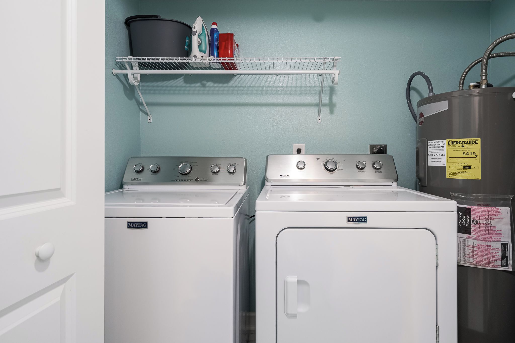 Un área de lavandería con dos lavadoras y secadoras Maytag, un estante metálico con productos de limpieza y un calentador de agua.