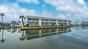 Un hôtel situé au bord de l’eau, avec un long bâtiment doté de balcons et dont l’image se reflète dans l’eau calme.