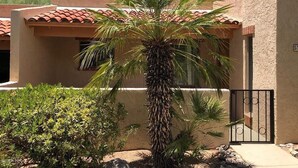 A building with a stucco exterior and red-tiled roof, surrounded by a palm tree and various shrubs. - The Perfect Tucson Townhome in Catalina Foothills (Tucson)