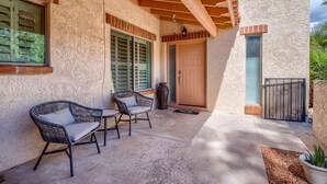 A covered patio with two wicker chairs and a table, a wooden door, and a small potted plant. - The Perfect Tucson Townhome in Catalina Foothills (Tucson)