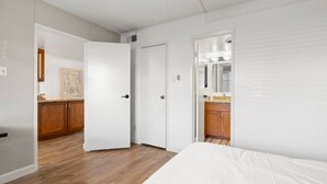 A bedroom with a bed, a door leading to a bathroom, and a kitchen area visible through an open door. - Lovely 2-Bedroom Apartment in Scottsdale! (Scottsdale)