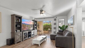 A spacious living room with a wooden floor, a white coffee table, a grey sofa, a TV on a wooden cabinet, and a ceiling fan. - Lovely 2-Bedroom Apartment in Scottsdale! (Scottsdale)
