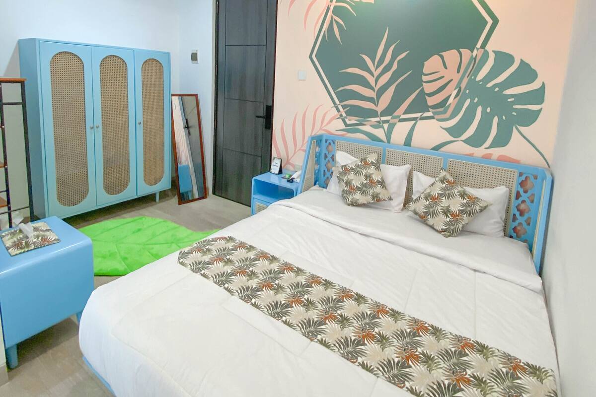 A bedroom with a bed, a wardrobe, a green rug, and a wall with a leaf pattern.