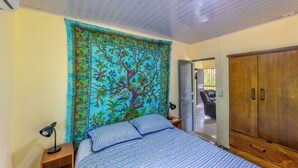 Quarto com cama, mesa de cabeceira, guarda-roupa de madeira e tapeçaria com desenho de árvore na parede.