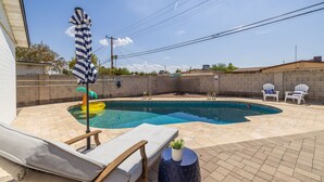 Un pati amb piscina, seients de relax i una taula petita amb una planta.