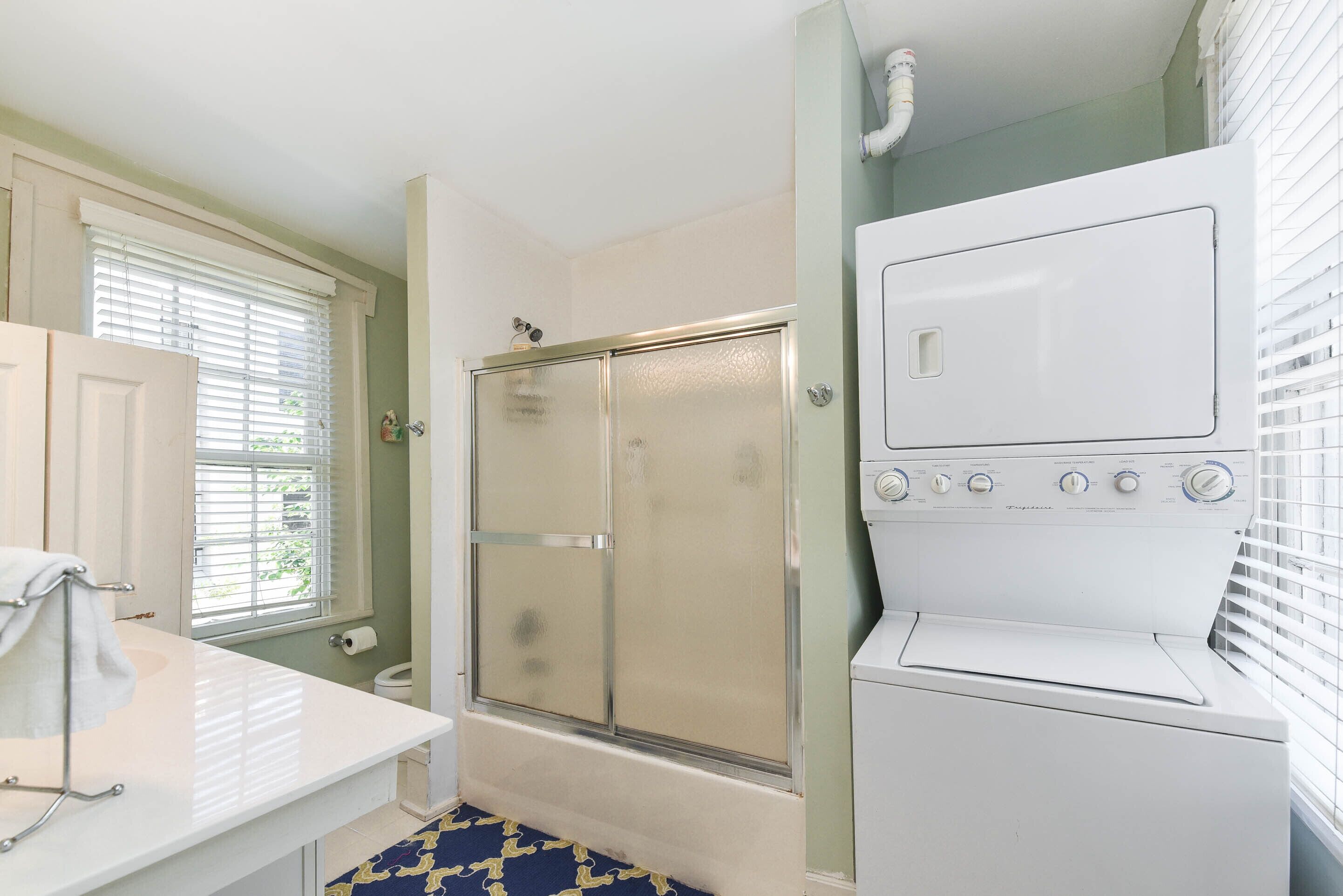 A bathroom with a white sink, a shower, and a front-loading washing machine.