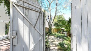 A white wooden gate leading to a pathway surrounded by greenery. - Artist's House Upper Apt Walk to Forsyth (Savannah)