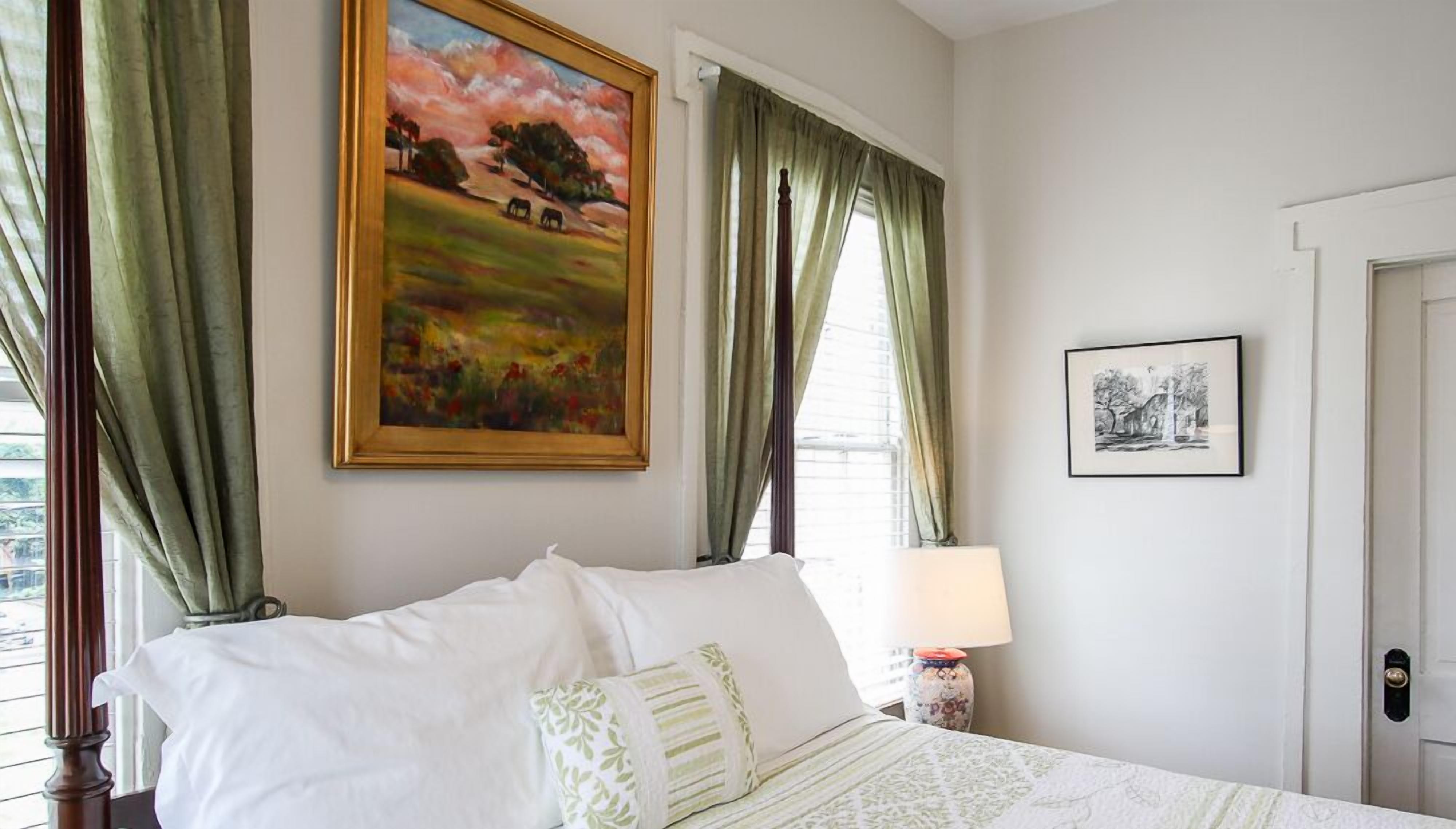 Une chambre à coucher avec un lit, des rideaux verts, un tableau, une lampe et une porte.