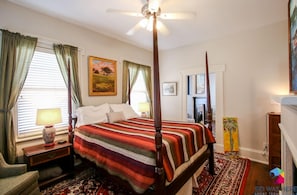 A four-poster bed with a striped bedspread, a ceiling fan, and a painting on the wall. - Artist's House Upper Apt Walk to Forsyth (Savannah)
