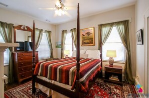 A four-poster bed with a striped bedspread, a wooden dresser, a nightstand with a lamp, and a painting on the wall. - Artist's House Upper Apt Walk to Forsyth (Savannah)