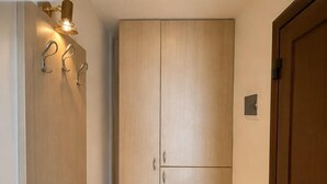 A hallway with a wooden wardrobe, a door with a vent, and a wall-mounted light fixture. - Avra Hotel (Thermaikos)