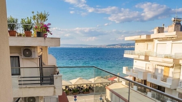 A balcony with a table and chairs, overlooking a coastal area with buildings and a clear sky. - Avra Hotel (Thermaikos)