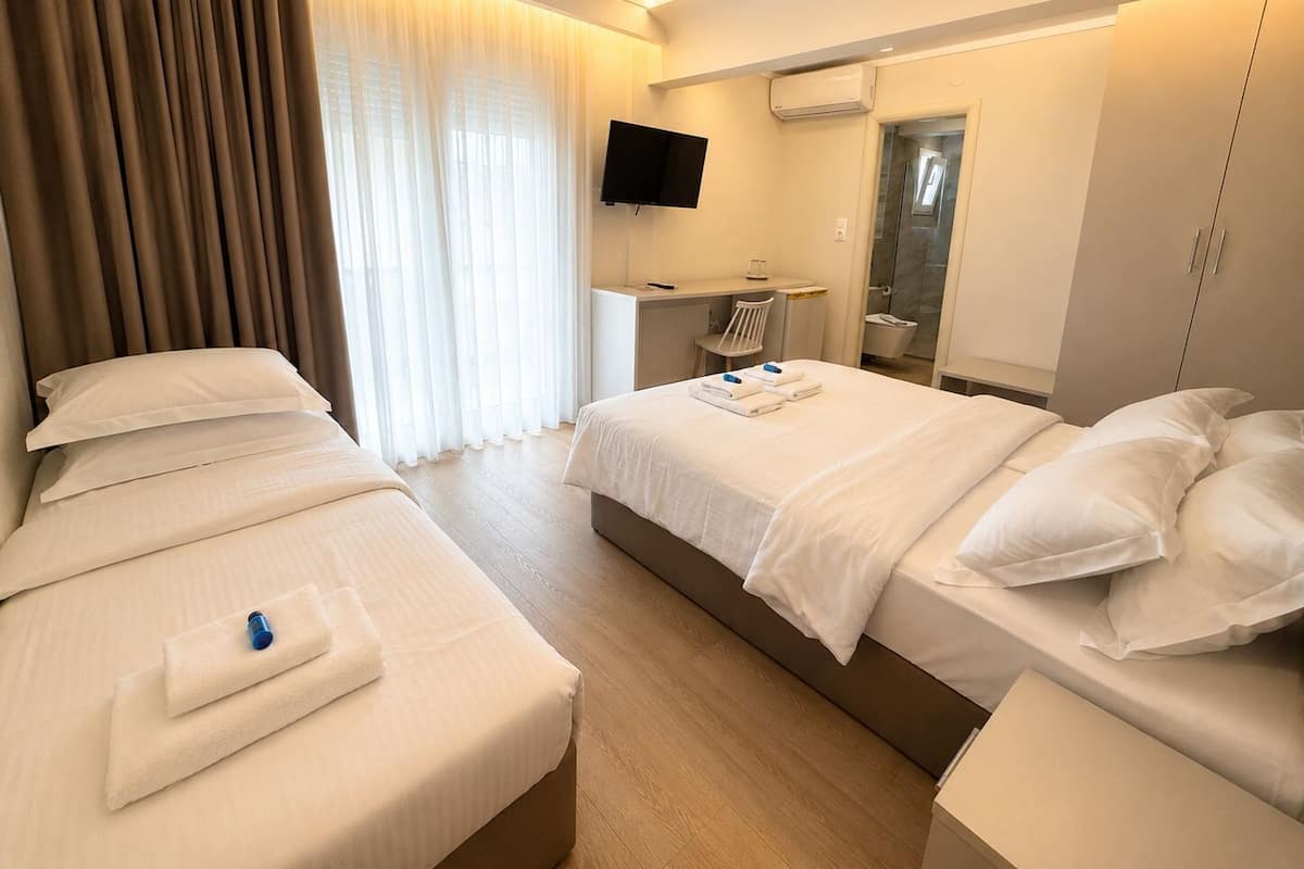 A hotel room with two beds, a desk, a TV, and a shower area.