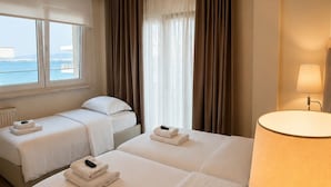 A hotel room with two beds, a window with a view, a lamp, and a radiator. - Avra Hotel (Thermaikos)