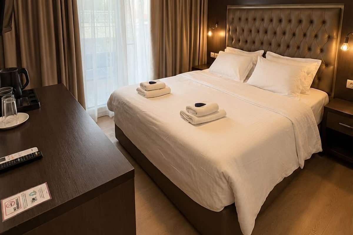 A hotel room with a large bed, a bedside table with a remote control, a coffee maker, and a nightstand with a lamp.