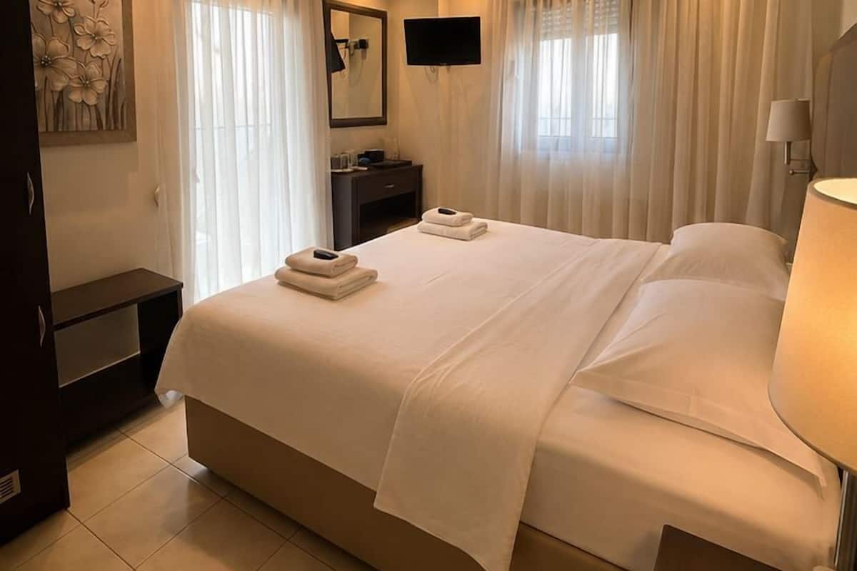 A hotel room with a large bed, a bedside table, a TV, and a wall-mounted air conditioner.