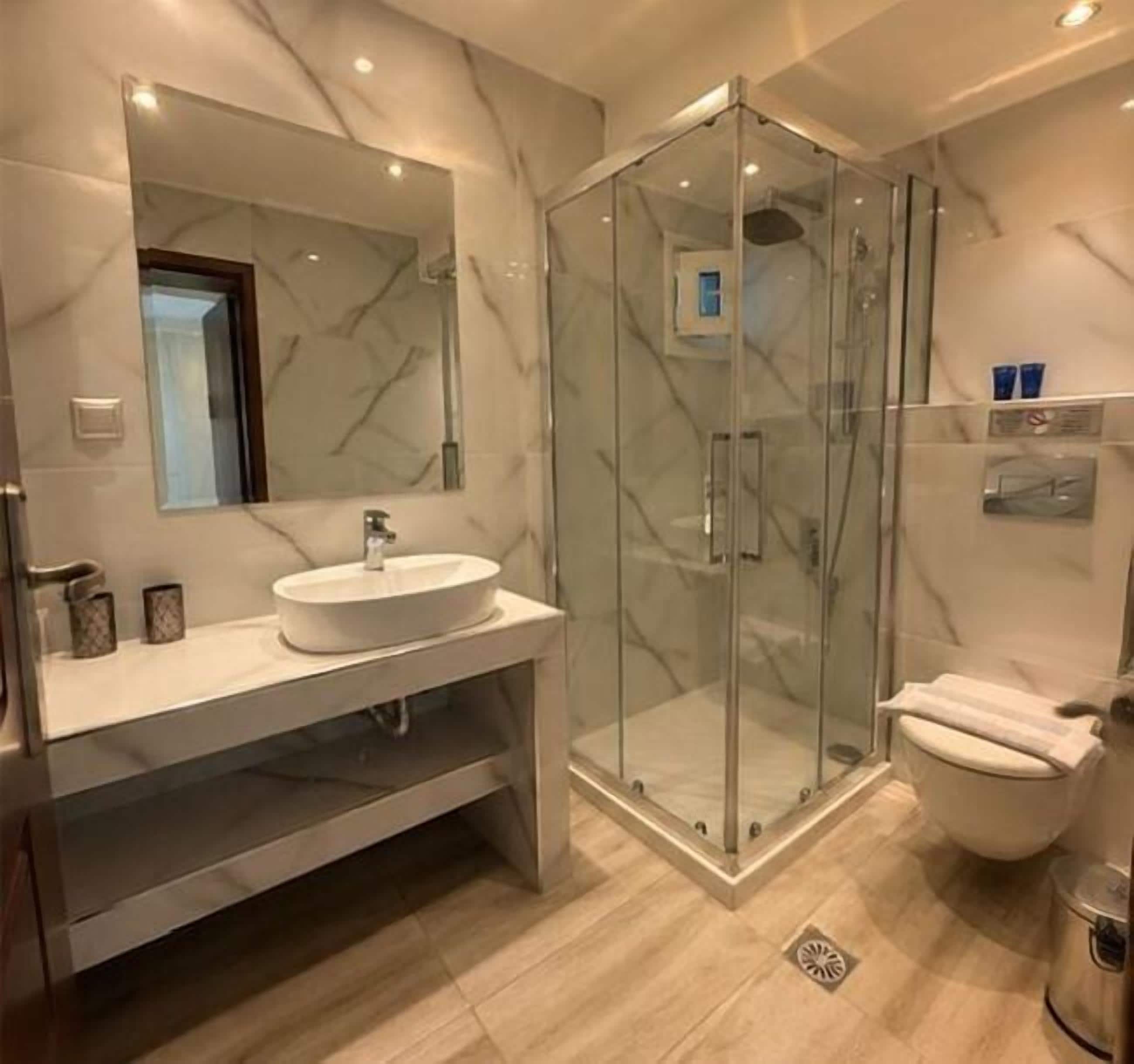 Un baño moderno con tocador de mármol, cabina de ducha de vidrio y un inodoro.