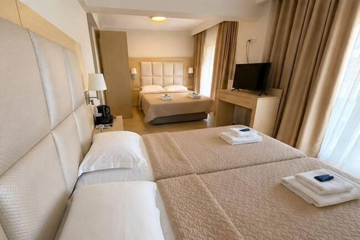 A hotel room with two beds, a TV, a desk, and a window with curtains.