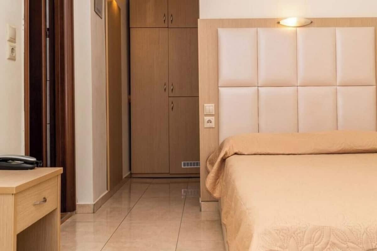 A hotel room with a bed, a wooden wardrobe, a bedside table, and a wall-mounted light.