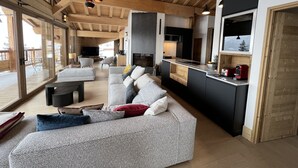 En rummelig opholdsstue med en stor sofa, et køkken med moderne design og store vinduer med udsigt til det fri.