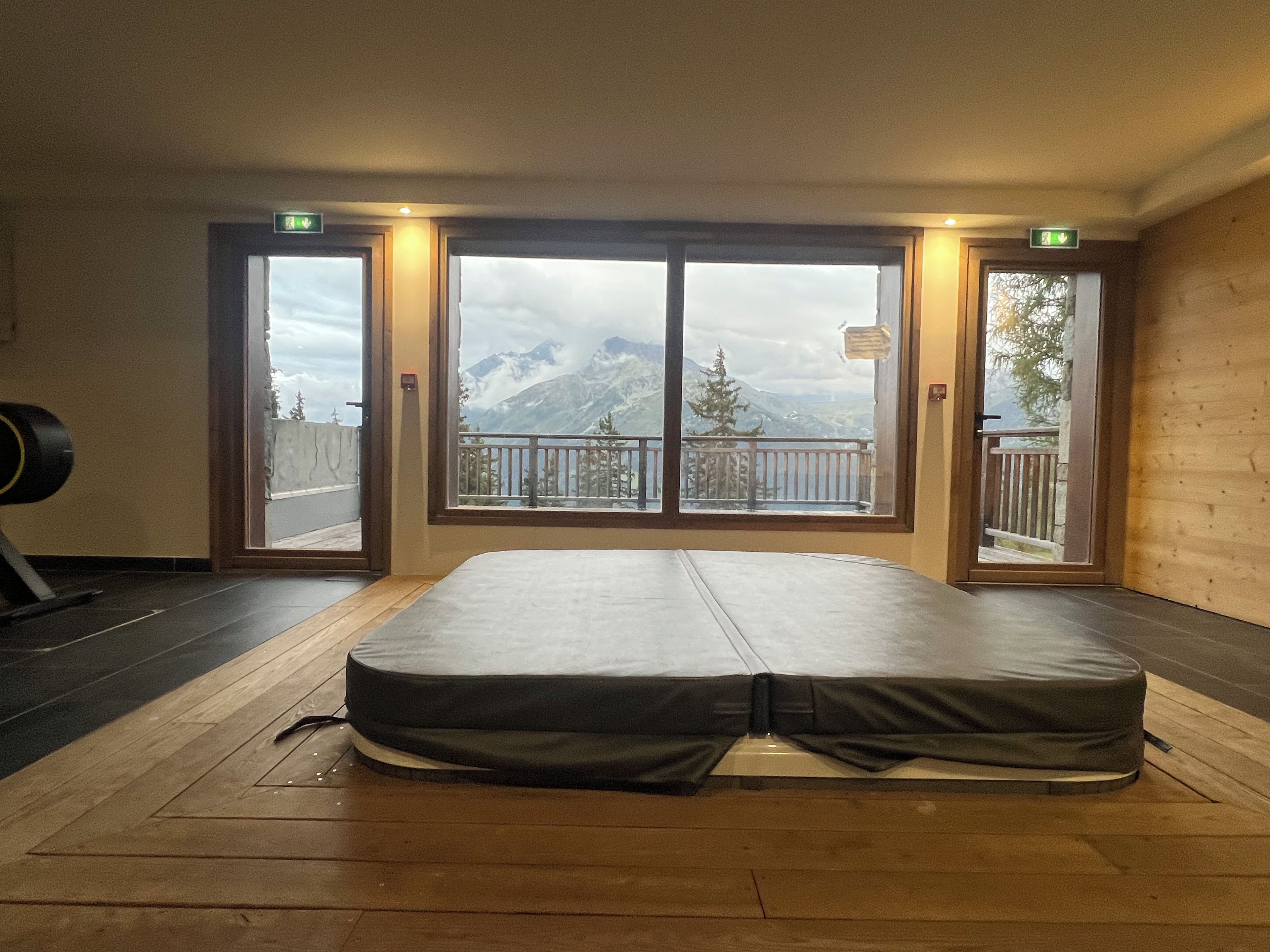 Een kamer met een groot bed, houten vloeren en uitzicht op bergen door een glazen deur.