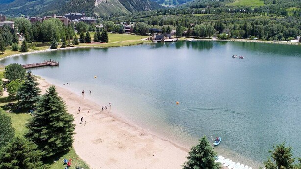 A lake with a sandy beach, surrounded by trees and buildings.