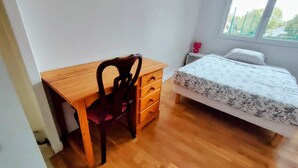 Ein Schlafzimmer mit einem Holztisch, einem Stuhl, einem Bett mit Blumenmuster, einem Nachttisch und einem Fenster.