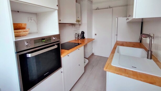 Eine kleine Küche mit weißen Schränken, einem eingebauten Backofen, einer Holz Arbeitsplatte und einem Spülbecken.