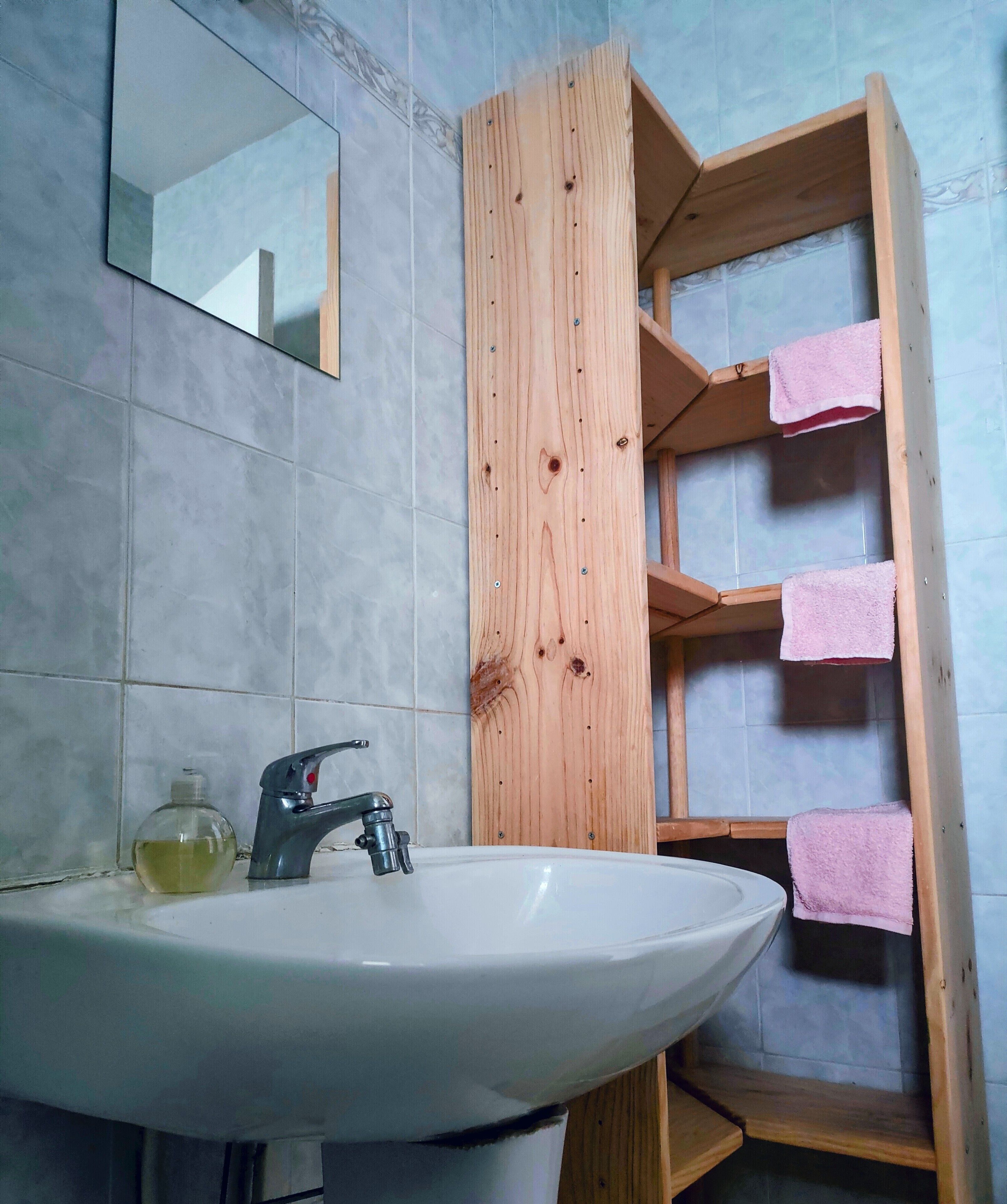 A bathroom with a white sink, a mirror, and a wooden shelf with pink towels.