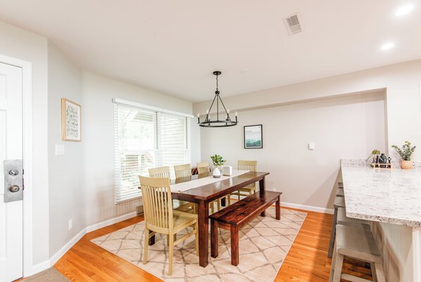 A dining area with a wooden table, chairs, and a bench. There is a chandelier above the table.