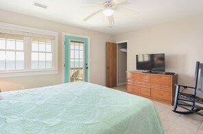 Une chambre à coucher avec un lit, un téléviseur posé sur une commode, une chaise et une porte donnant sur un balcon.
