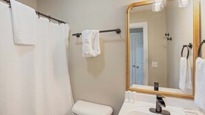 A bathroom with a white toilet, a towel rack with a towel, a shower curtain, and a large mirror with lights. - Peaceful Getaway, Sleeps 6・Hot Tub (Sevierville)