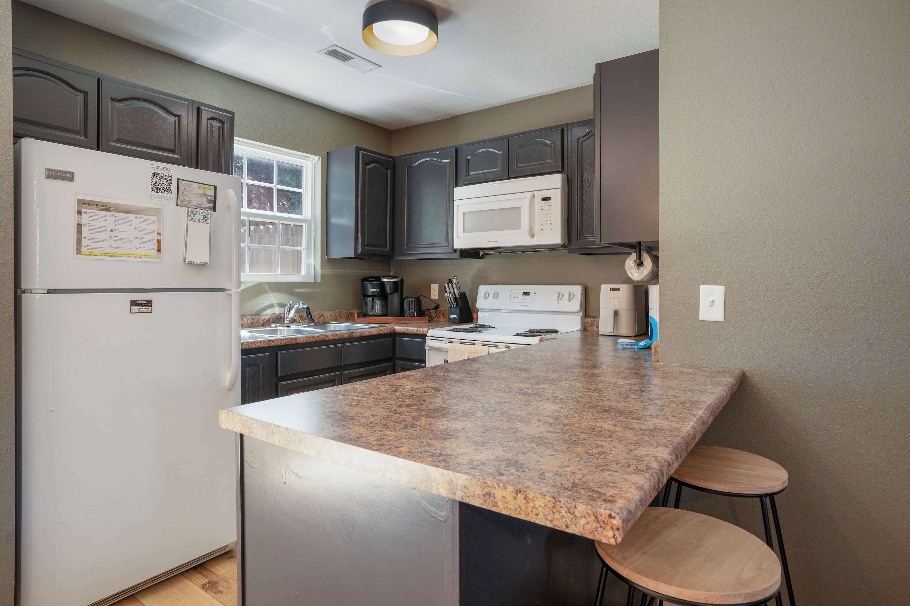 A kitchen with a central island, dark cabinets, a white refrigerator, a microwave, and a stove.