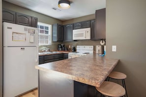 A kitchen with a central island, dark cabinets, a white refrigerator, a microwave, and a stove. - Sevierville Family Retreat with Private Hot Tub and Mountain Fun (Sevierville)