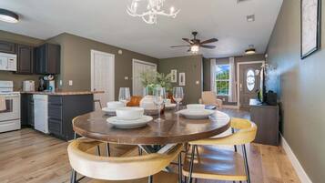 A modern kitchen with a dining area, featuring a round wooden table, yellow chairs, and a chandelier.