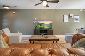 A living room with leather sofas, a coffee table, a television on a stand, and framed pictures on the wall. - Sevierville Family Retreat with Private Hot Tub and Mountain Fun (Sevierville)