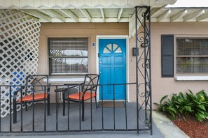 A blue door with a small window above it, a metal gate, and two chairs with orange cushions.