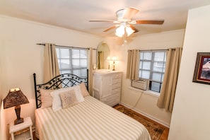 A bedroom with a bed, a dresser, a mirror, a ceiling fan, and two windows with curtains.