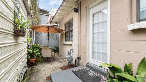 A small outdoor patio area with a table and chairs, a potted plant, and a welcome mat.