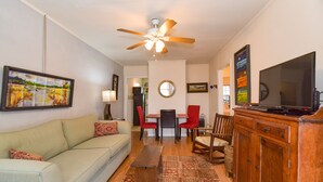 A living room with a sofa, a coffee table, a TV, a ceiling fan, and a dining area with chairs and a table.