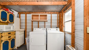 A compact laundry room with two stacked washers and dryers, wooden cabinets, and a window.