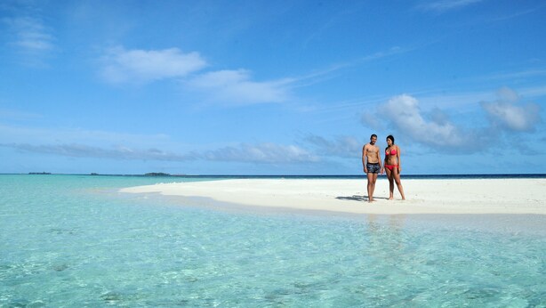 A couple standing on a white sandy beach with clear turquoise water. - Arianna Dhangethi (Dhangethi)