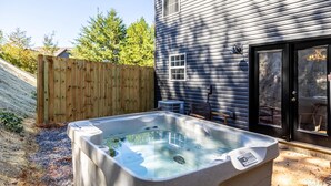 A hot tub in a backyard with a wooden fence, a house with a black door, and a window with a view of trees. - Peaceful Getaway, Sleeps 6・Pet Friendly & Hot Tub (Sevierville)