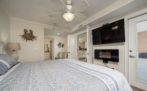 Une chambre dotée d’un grand lit, d’un ventilateur de plafond, d’un téléviseur à écran plat fixé au mur et d’une porte donnant accès à une salle de bain.