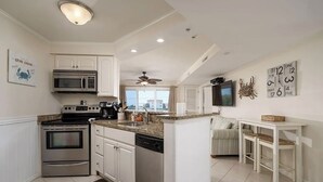 Una cocina moderna con electrodomésticos de acero inoxidable, un comedor con mesa y sillas blancas, y vistas a la ciudad a través de amplios ventanales.